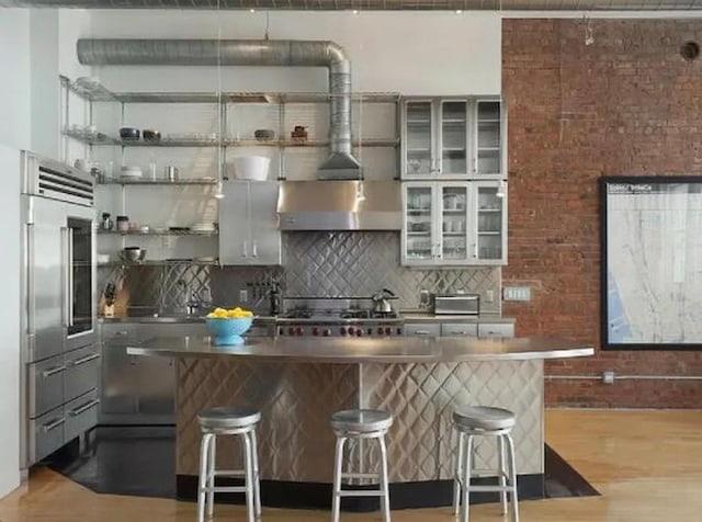 kitchen featuring built in fridge, light wood-type flooring, tasteful backsplash, and a kitchen breakfast bar