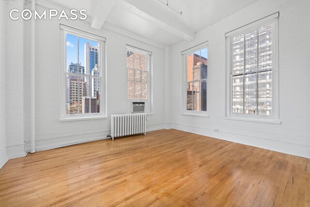 448 W 37th St Unit 6H, New York City, NY 10018 - spare room with radiator heating unit, wood finished floors, beam ceiling, and a view of city