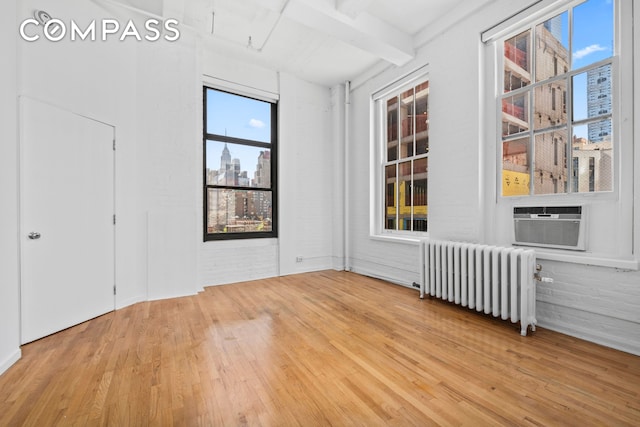 448 W 37th St Unit 6H, New York City, NY 10018 - empty room featuring radiator heating unit, wood finished floors, beamed ceiling, attic access, and a city view
