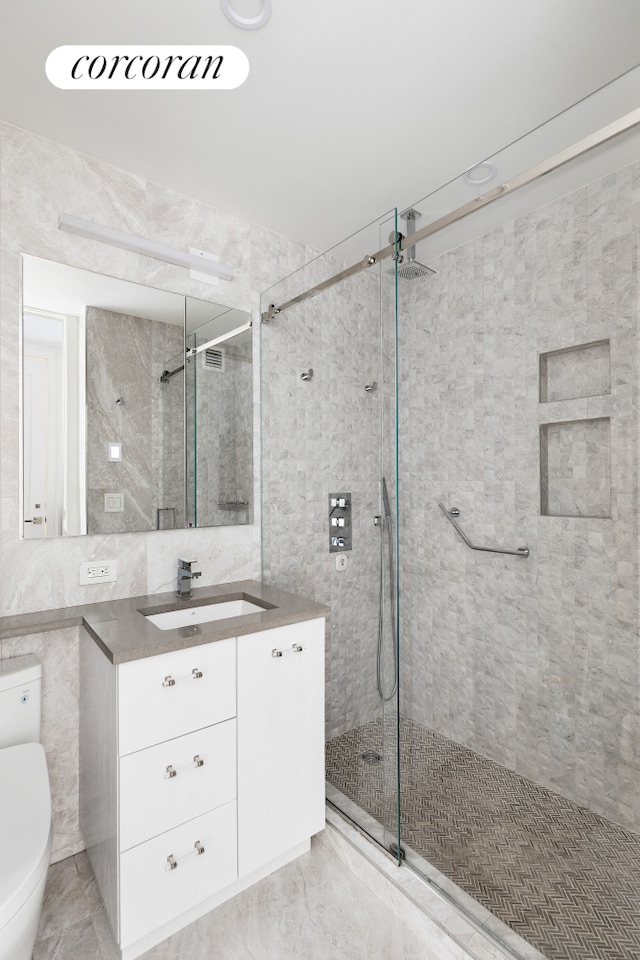 bathroom with toilet, tile walls, a shower stall, and vanity