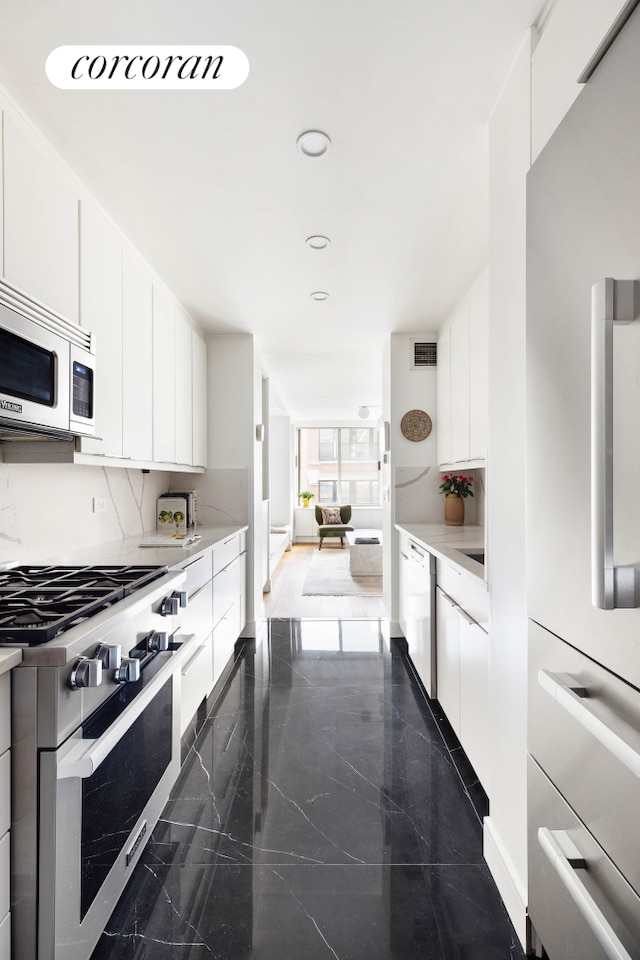 kitchen featuring stainless steel appliances, tasteful backsplash, granite tiled floors, white cabinetry, and recessed lighting