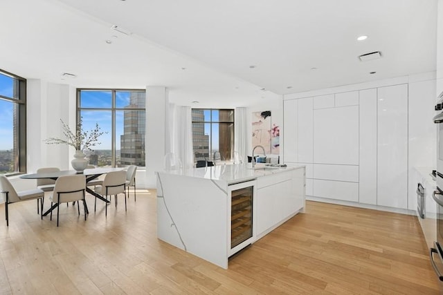 75 Wall St Unit Phd2, New York City, NY 10005 - kitchen featuring modern cabinets, beverage cooler, a sink, light wood-style floors, and white cabinets