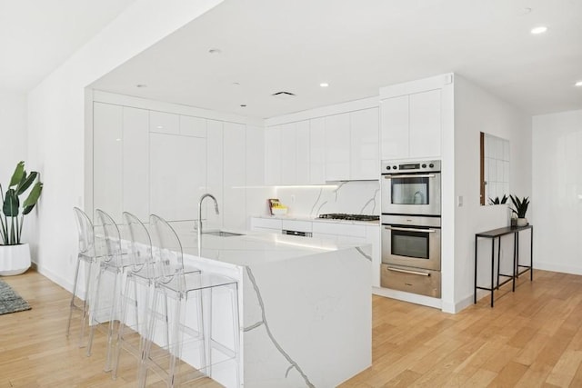75 Wall St Unit Phd2, New York City, NY 10005 - kitchen with double oven, a warming drawer, light wood-style flooring, white cabinets, and a kitchen bar