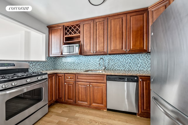 kitchen featuring stainless steel appliances, a sink, light stone counters, and light wood-style floors