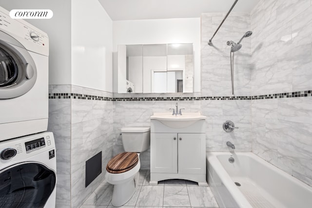 full bath featuring stacked washer / drying machine, tub / shower combination, toilet, tile walls, and vanity