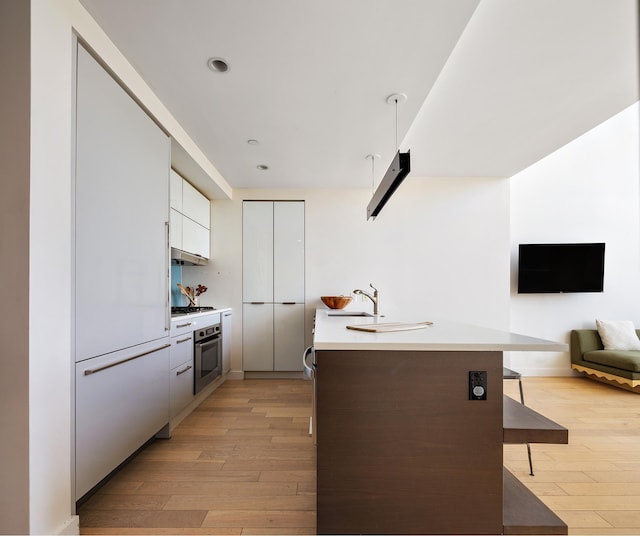 kitchen featuring stainless steel oven, light wood-type flooring, modern cabinets, white cabinets, and light countertops