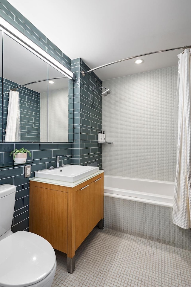 bathroom with tile walls, tiled shower / bath, toilet, tile patterned flooring, and vanity