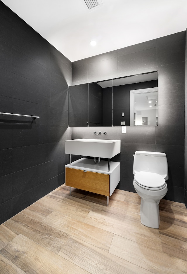 318 E 81st St Unit 1, New York City, NY 10028 - half bathroom featuring toilet, vanity, tile walls, and wood finished floors