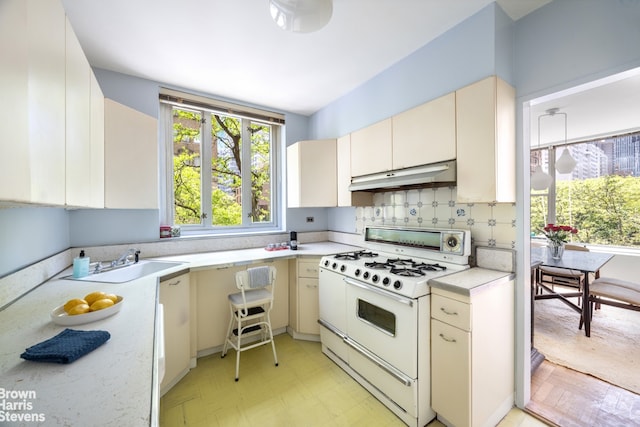 kitchen with white range with gas cooktop, under cabinet range hood, cream cabinetry, light countertops, and a sink