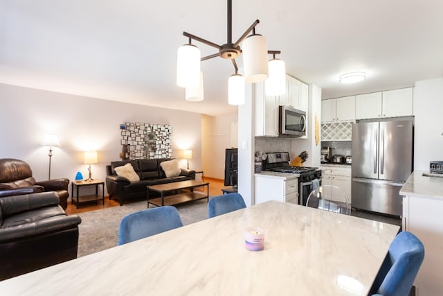 kitchen with stainless steel appliances, open floor plan, white cabinetry, backsplash, and decorative light fixtures