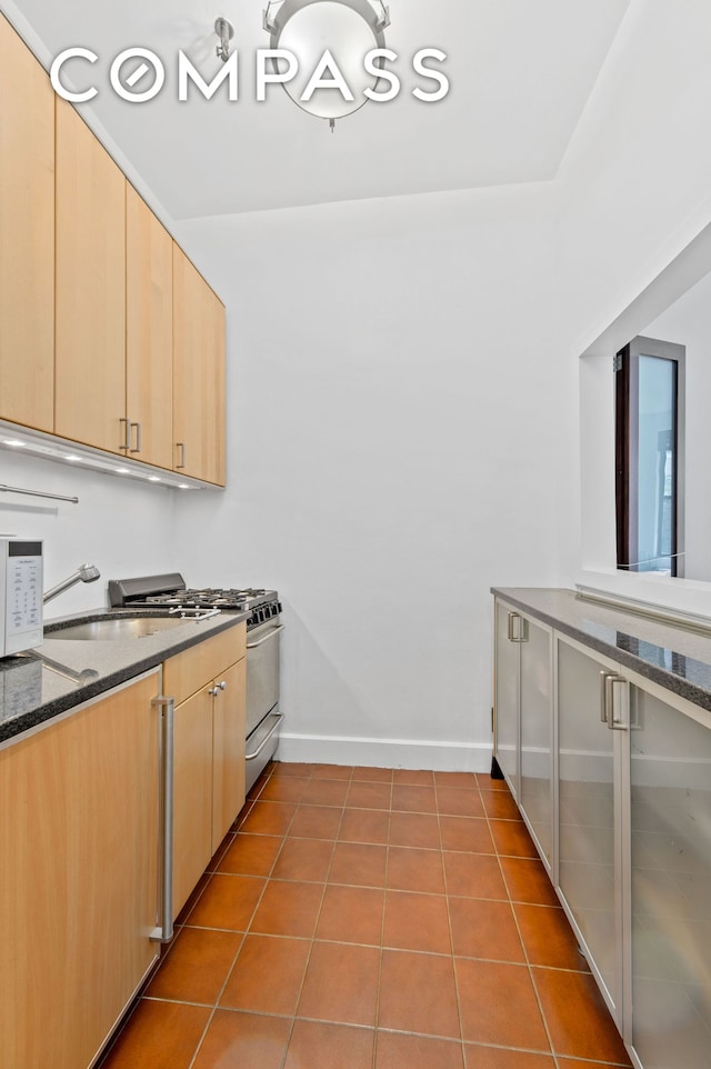 340 E 83rd St Unit 1A, New York City, NY 10028 - kitchen featuring gas range, light brown cabinetry, dark stone counters, baseboards, and tile patterned floors