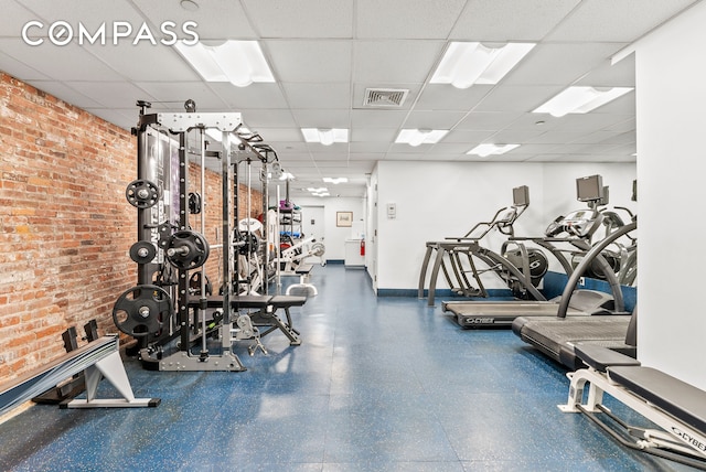 gym with a paneled ceiling, brick wall, and baseboards