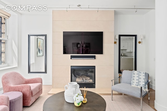 living room with a tiled fireplace, track lighting, wood finished floors, and baseboards