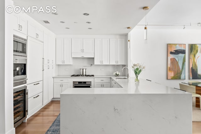 kitchen featuring appliances with stainless steel finishes, a sink, light wood finished floors, wine cooler, and white cabinetry