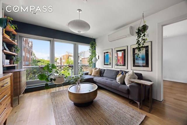 living room with an AC wall unit, light wood-style flooring, a city view, and baseboards