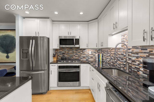 kitchen featuring appliances with stainless steel finishes, a sink, white cabinetry, dark stone countertops, and backsplash
