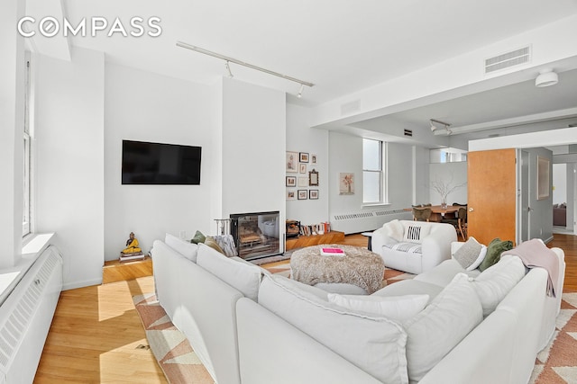 35 E 12th St Unit 8C, New York City, NY 10003 - living room with rail lighting, radiator, light wood-type flooring, and a glass covered fireplace
