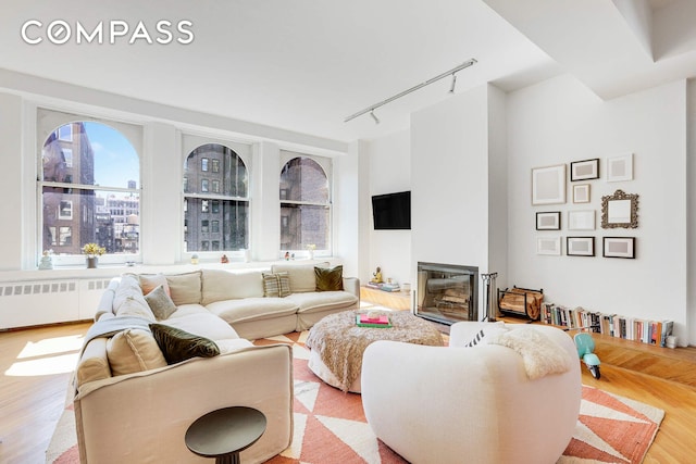 35 E 12th St Unit 8C, New York City, NY 10003 - living room featuring rail lighting, wood finished floors, a glass covered fireplace, and radiator heating unit