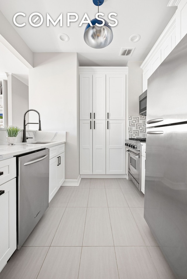 kitchen with appliances with stainless steel finishes, a sink, white cabinets, light tile patterned floors, and light stone countertops