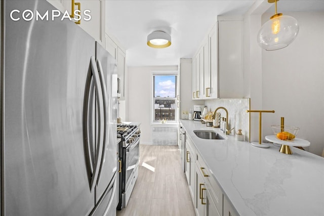 kitchen featuring stainless steel appliances, a sink, light stone countertops, and white cabinets