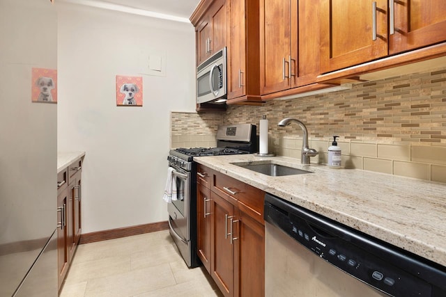 kitchen with appliances with stainless steel finishes, a sink, brown cabinets, light stone countertops, and tasteful backsplash