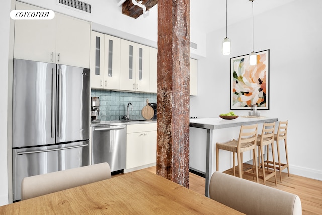124 W 24th St Unit 4B, New York City, NY 10011 - kitchen featuring appliances with stainless steel finishes, light wood-style floors, backsplash, and white cabinetry