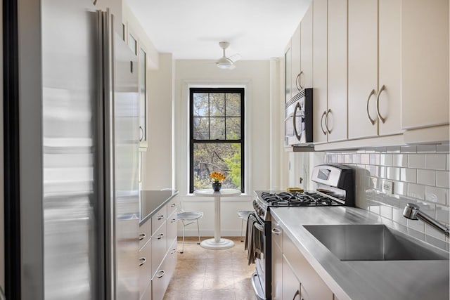 kitchen featuring appliances with stainless steel finishes, tasteful backsplash, a sink, white cabinetry, and baseboards