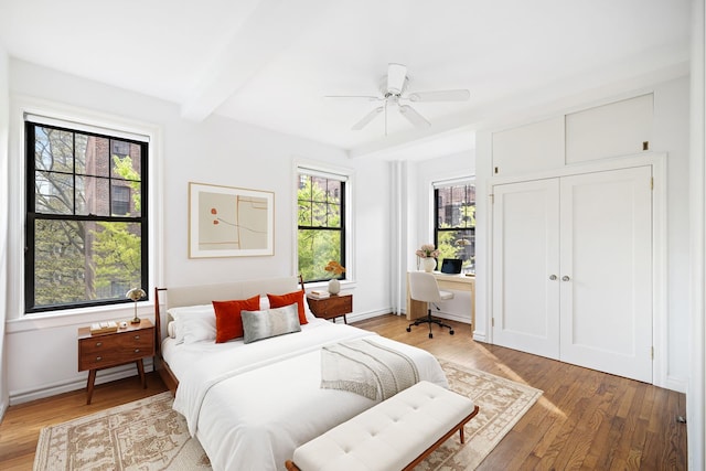 bedroom with light wood-type flooring, a desk, beam ceiling, a ceiling fan, and baseboards