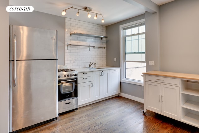 kitchen featuring appliances with stainless steel finishes, open shelves, a sink, backsplash, and white cabinetry