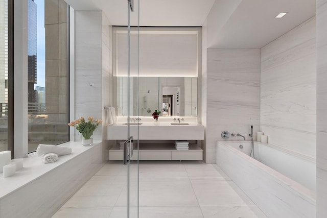bathroom featuring a garden tub, vanity, tile walls, and marble finish floors