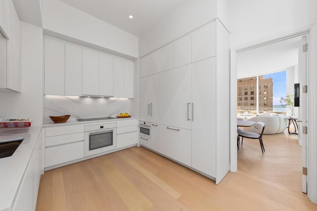 kitchen featuring white oven, light countertops, light wood finished floors, and white cabinetry