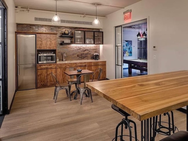 bar featuring stainless steel appliances, light wood finished floors, a sink, and hanging light fixtures