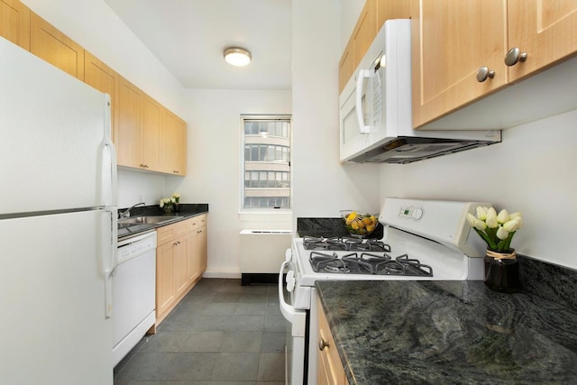 kitchen featuring white appliances, light brown cabinets, dark tile patterned flooring, dark stone countertops, and a sink