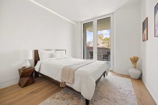bedroom with access to exterior, floor to ceiling windows, light wood-type flooring, and baseboards