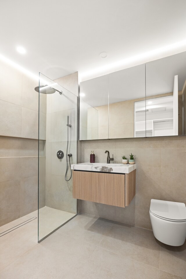 bathroom with tile walls, tile patterned floors, a walk in shower, toilet, and vanity
