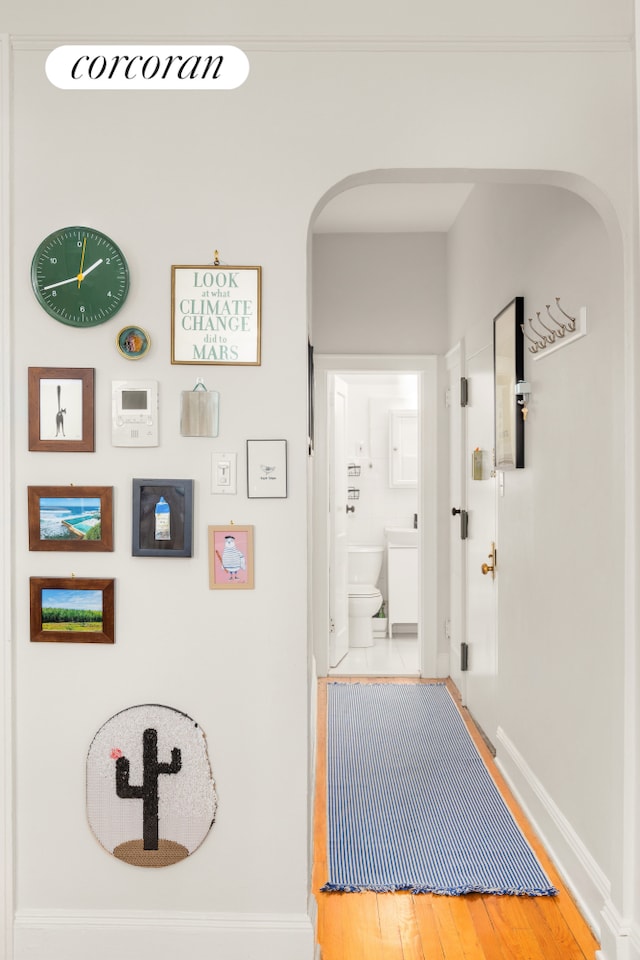 corridor with arched walkways, wood finished floors, and baseboards