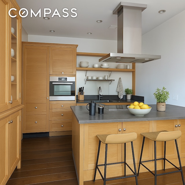 kitchen with stainless steel oven, island range hood, a sink, a breakfast bar area, and open shelves