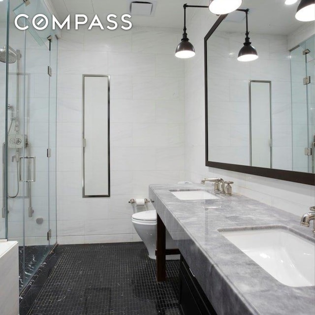 425 W 50th St Unit 15G, New York City, NY 10019 - bathroom with tile walls, a stall shower, double vanity, toilet, and tile patterned floors