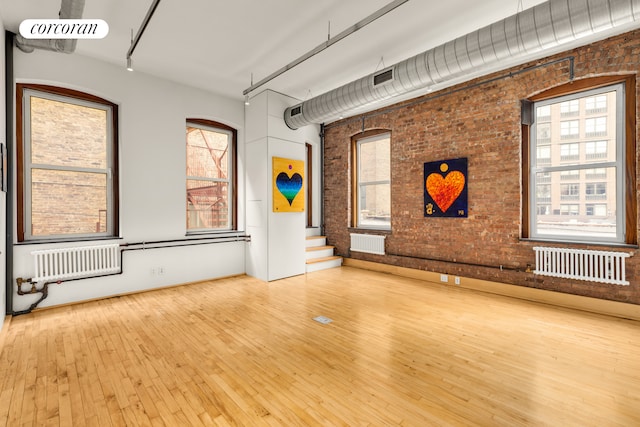 25 E 4th St Unit 2, New York City, NY 10003 - unfurnished living room featuring brick wall, wood-type flooring, plenty of natural light, stairs, and radiator heating unit