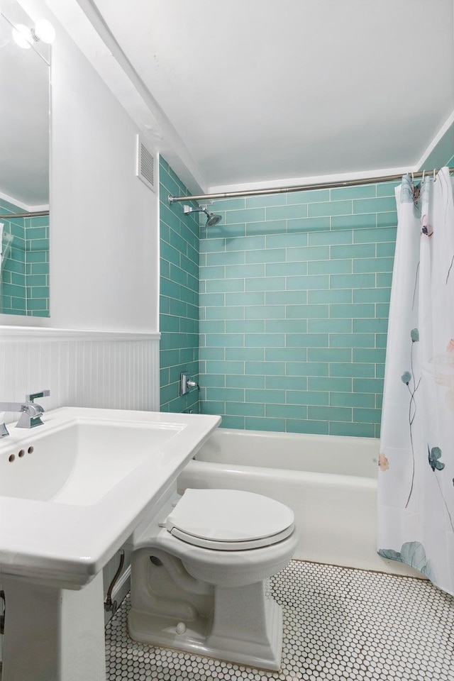 full bathroom with tile patterned floors, toilet, shower / bath combination with curtain, and wainscoting