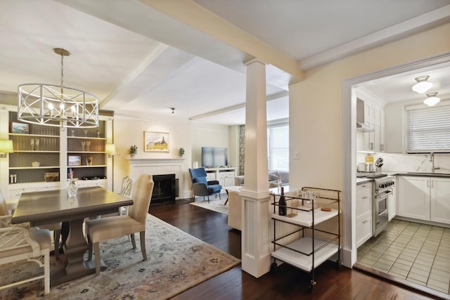 dining room with dark wood-style floors, a chandelier, a fireplace, and ornate columns