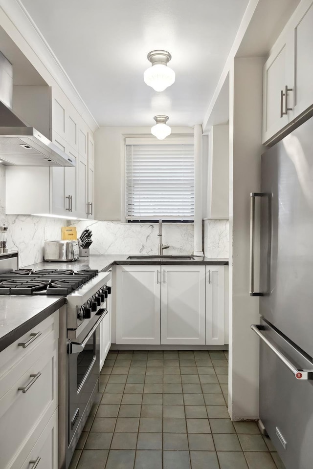 kitchen with appliances with stainless steel finishes, a sink, tile patterned floors, wall chimney range hood, and backsplash