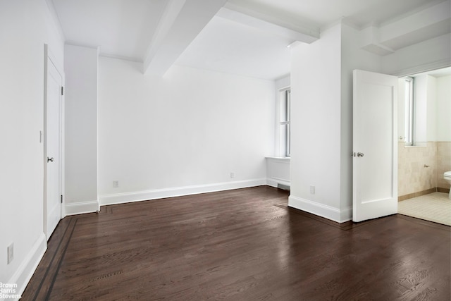 spare room featuring beamed ceiling, dark wood-type flooring, and baseboards