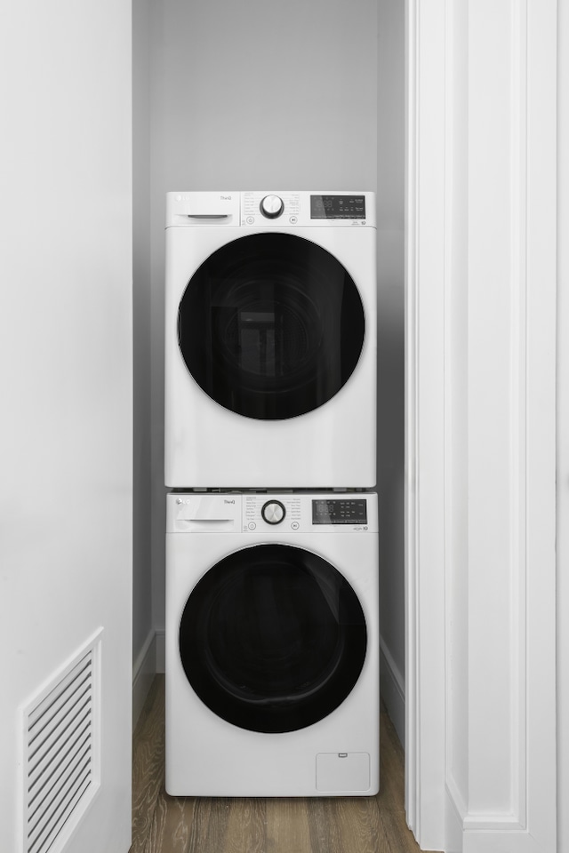 clothes washing area with stacked washer / dryer, wood finished floors, and baseboards