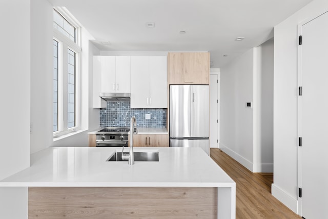 kitchen with stainless steel fridge, a sink, under cabinet range hood, decorative backsplash, and light countertops