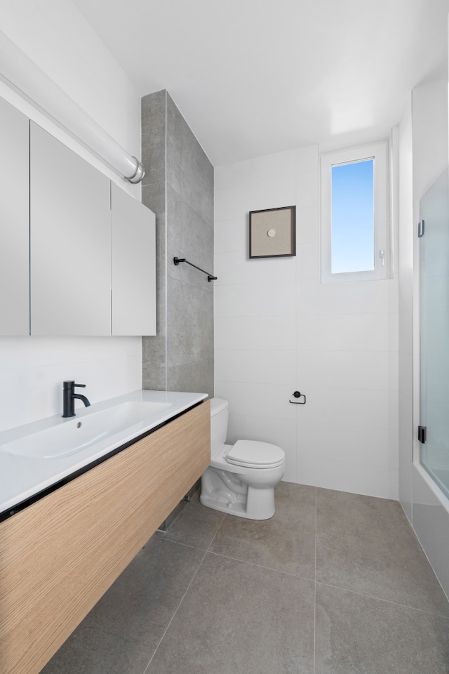 bathroom featuring toilet, a shower with door, tile patterned flooring, a sink, and tile walls