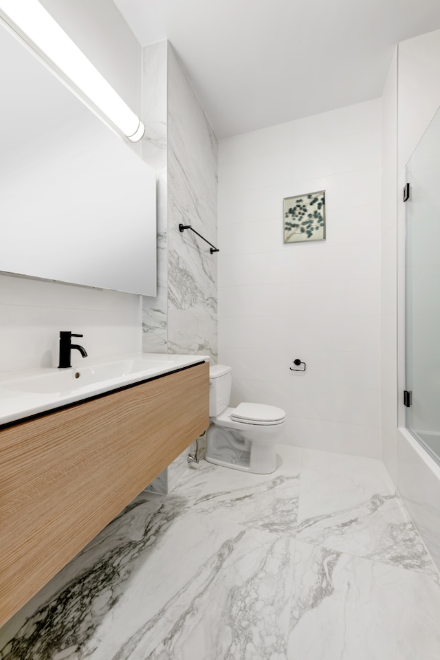 bathroom featuring toilet, marble look tile flooring, vanity, and tile walls