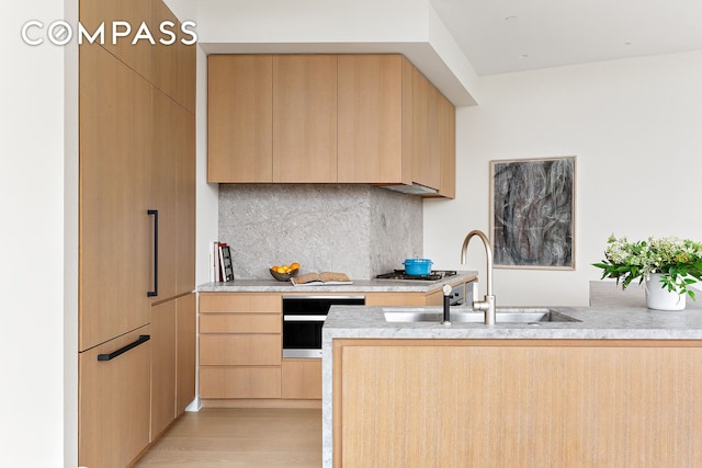 kitchen featuring light brown cabinetry, a sink, modern cabinets, backsplash, and light countertops