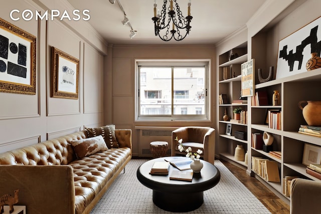 living area featuring radiator heating unit, a decorative wall, built in features, a chandelier, and crown molding