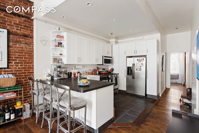 138 W 73rd St, New York City, NY 10023 - kitchen featuring stainless steel appliances, dark countertops, a peninsula, open shelves, and white cabinetry